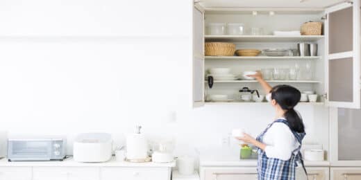 Woman arranging dishes and glasses in neatly organized kitchen cabinets, illustrating an efficient system for decluttering and following 7 steps for organizing kitchen cabinets.