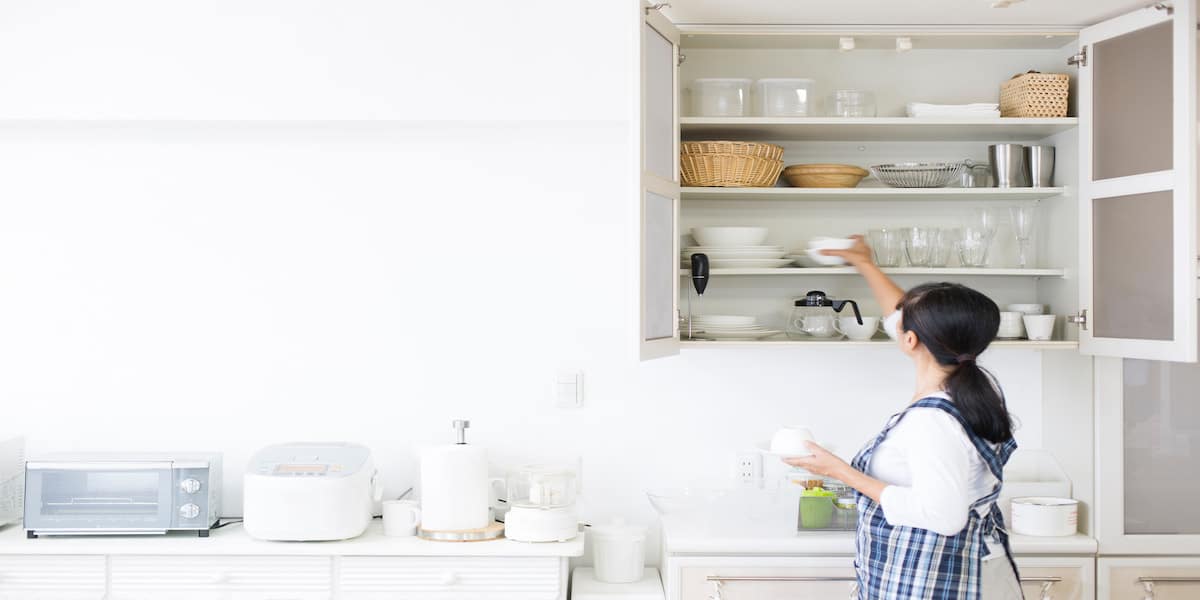 Woman arranging dishes and glasses in neatly organized kitchen cabinets, illustrating an efficient system for decluttering and following 7 steps for organizing kitchen cabinets.