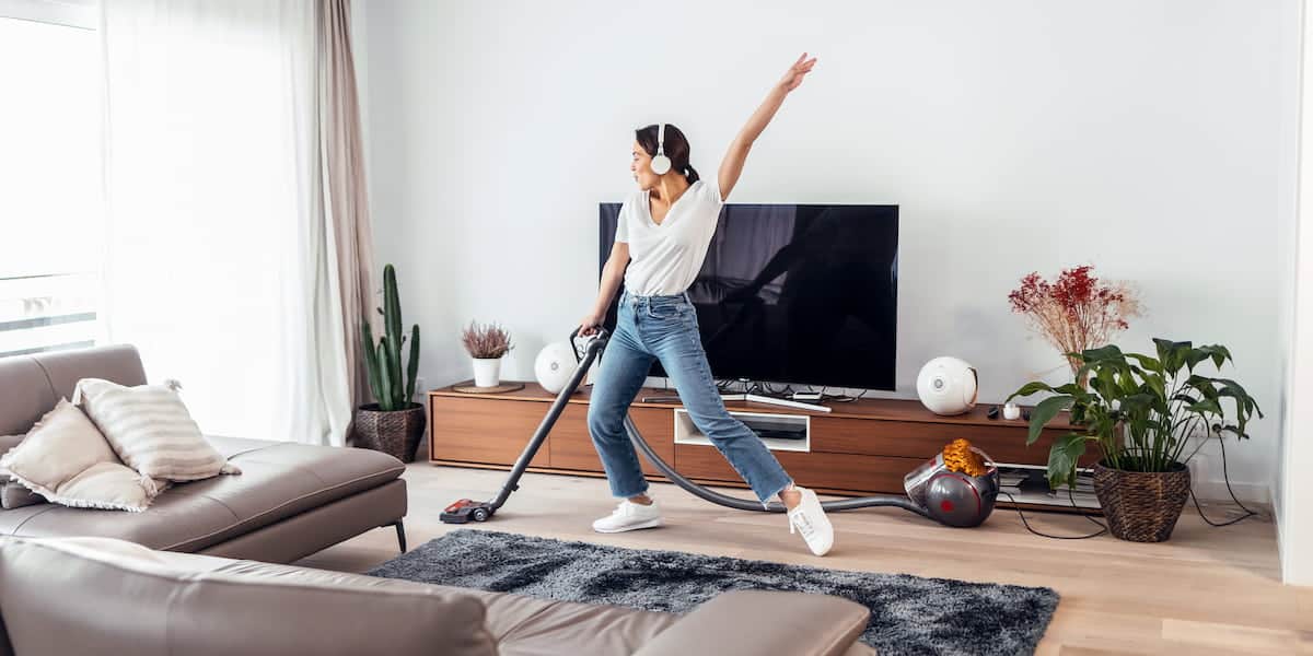 A woman vacuuming her living room with headphones on, showcasing the benefits of a clean home, including a tidy, organized, and inviting space.