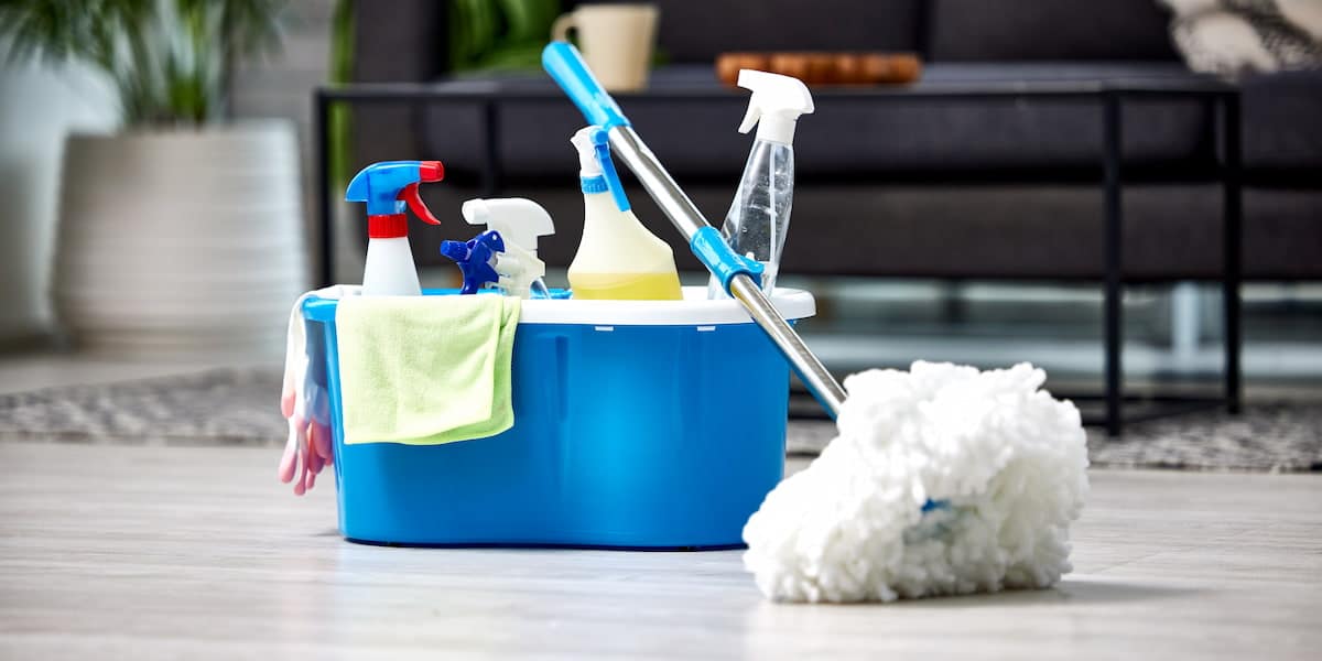 A blue cleaning bucket filled with spray bottles, a mop, and microfiber cloths, representing essential tools for effective house cleaning tips.