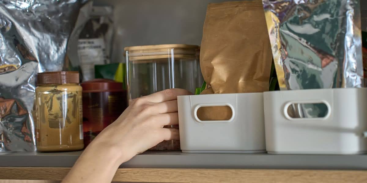 Hand reaching into pantry with jars, bags, and bins showing practical tips on how to organize a pantry for efficient food storage