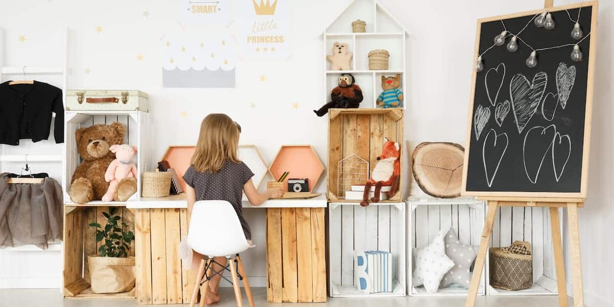 A stylish and functional kids' room with creative storage solutions, featuring wooden crates, shelves, and a chalkboard. The space is designed with practical and aesthetic 'kids room storage' options, including cubbies for toys, books, and decorative items