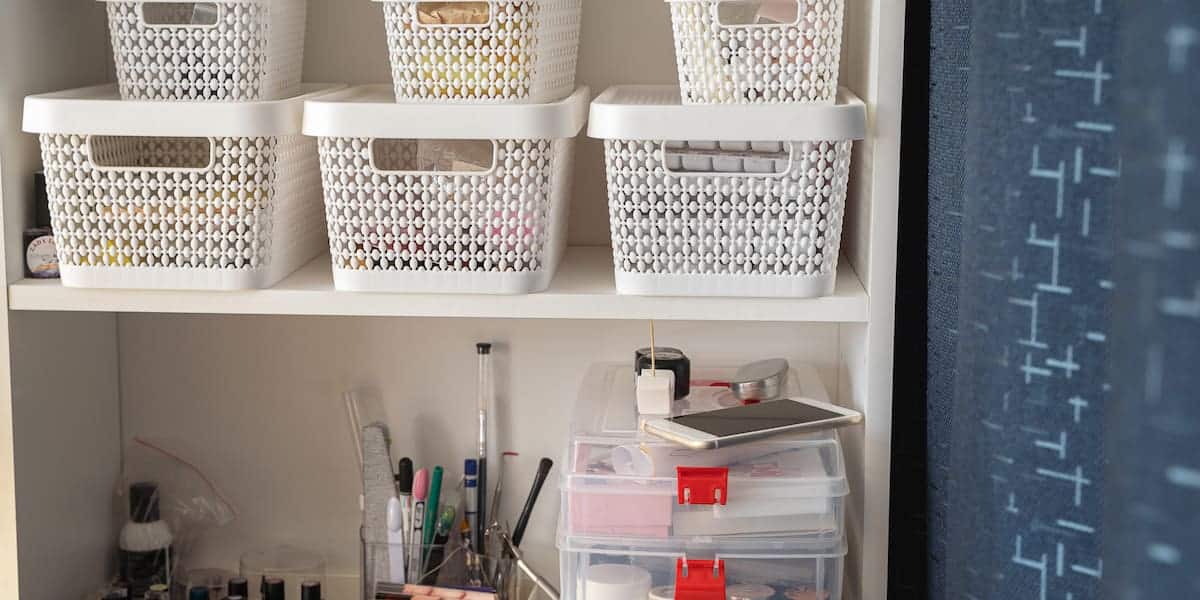 Organized shelving unit showcasing various storage solutions for small spaces, including stackable white plastic baskets with lids and clear plastic drawers with red clips, ideal for compact and efficient organization.